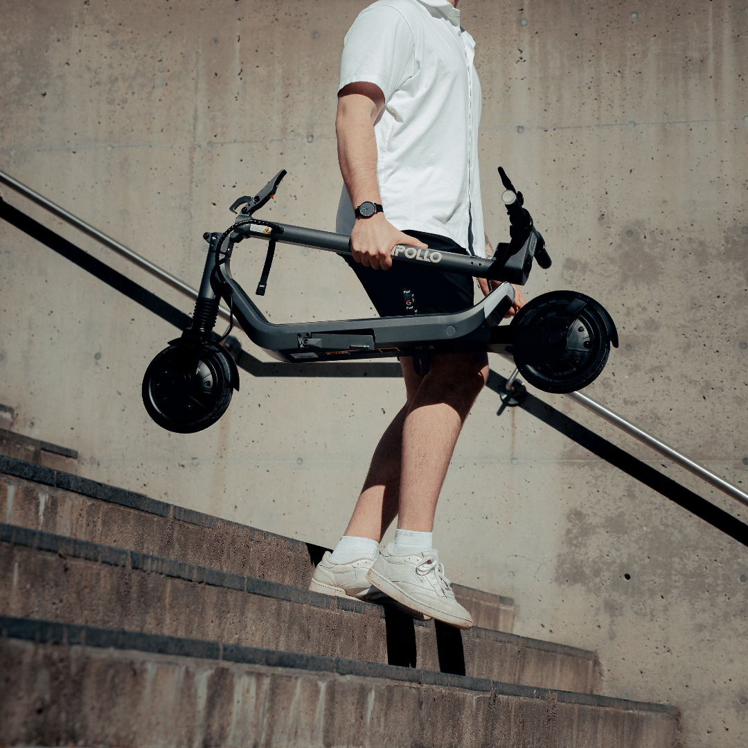 Person carrying a black electric scooter up a set of stairs.