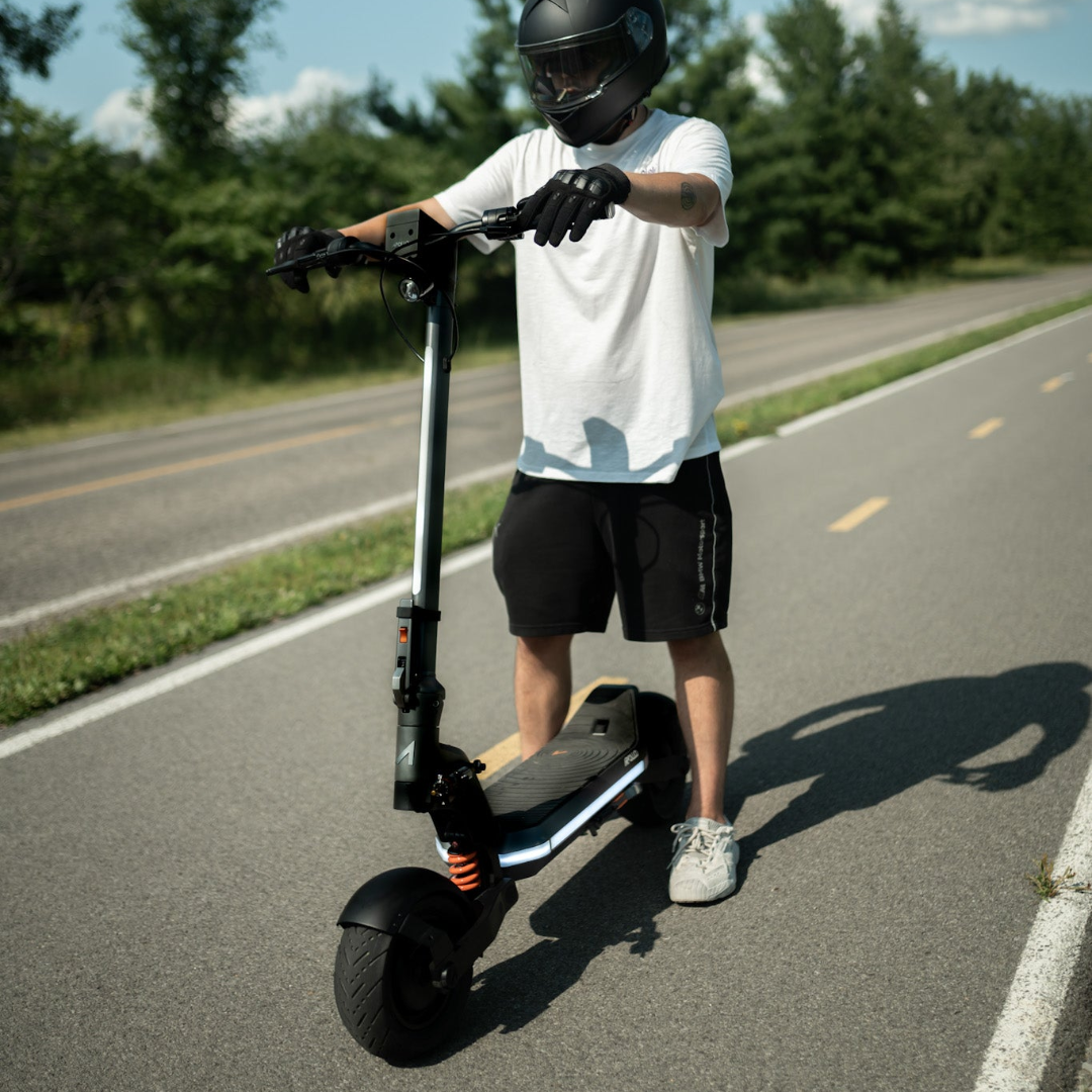 Person riding an electric scooter on a road with trees in the background