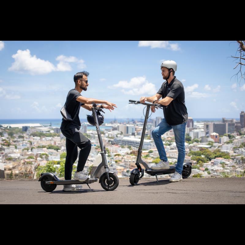 two men facing each other while stopped on their Apollo e-scooters with the city horizon behind them