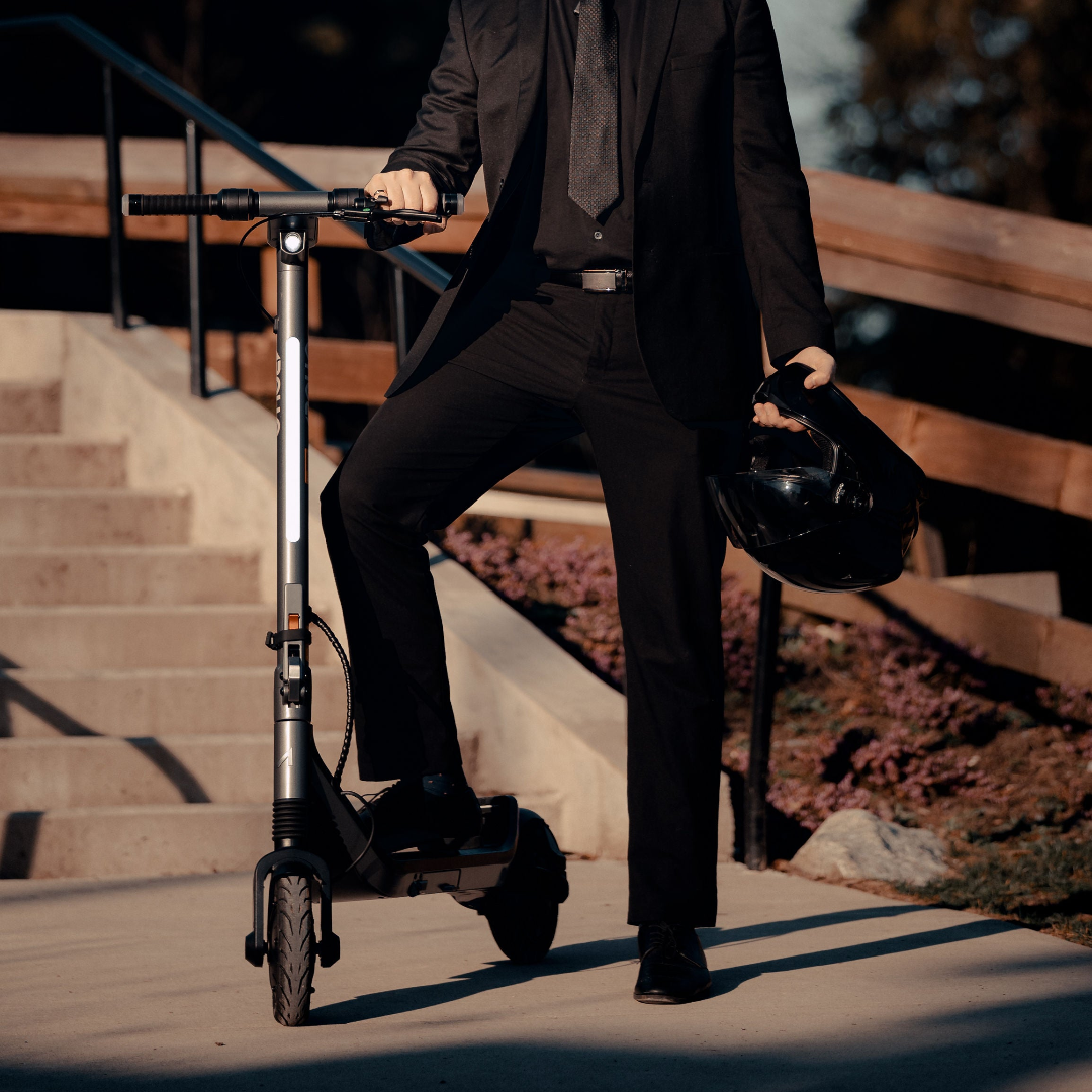 Person in a black suit standing beside an Apollo Go electric scooter with a helmet in hand, outdoors.