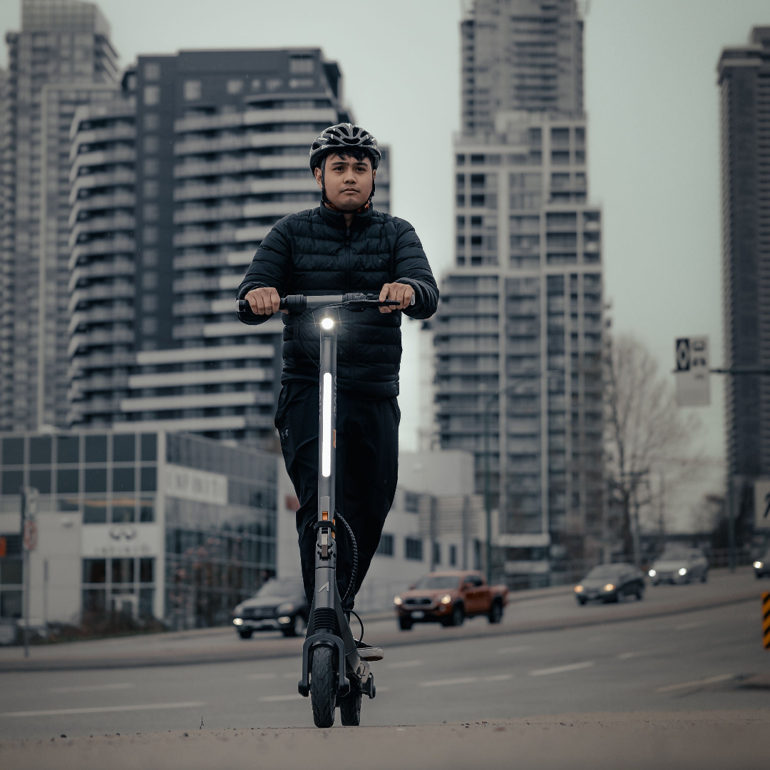 Person riding an Apollo Go electric scooter on a city street with tall buildings in the background